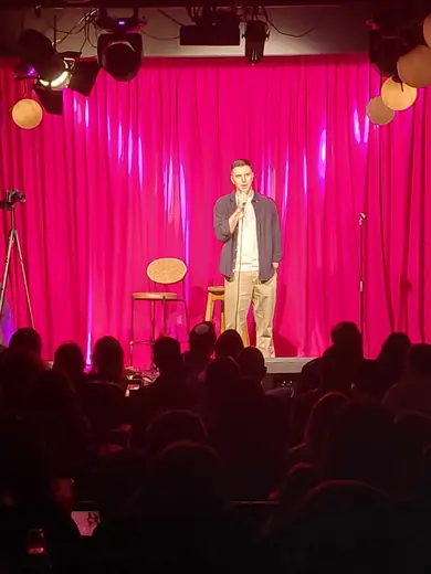 Dovi Neuburger on a pink-lit comedy stage